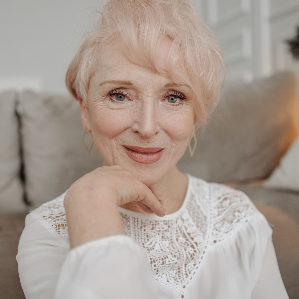 Elegant senior woman smiling warmly while posing in comfortable indoor setting.